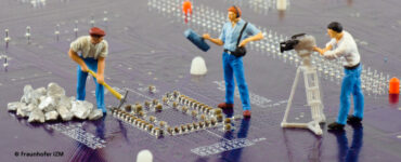 Circuit board with miniature construction workers and camera crew, Fraunhofer IZM