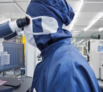 An employee in front of a microscope in the clean room (c) Fraunhofer IZM I Volker Mai