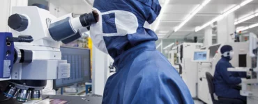 An employee in front of a microscope in the clean room (c) Fraunhofer IZM I Volker Mai