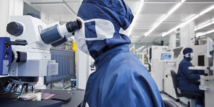 An employee in front of a microscope in the clean room (c) Fraunhofer IZM I Volker Mai