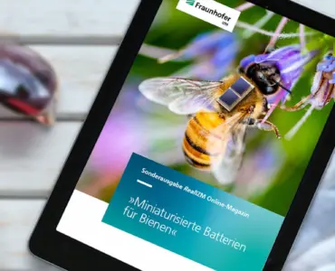 Tablet mit dem Titelbild des RealIZM Online-Magazins auf einem Steck mit Sonnenbrille, Cocktail und Pflanze | © Fraunhofer IZM | Volker Mai | MargJohnsonVA – stock.adobe