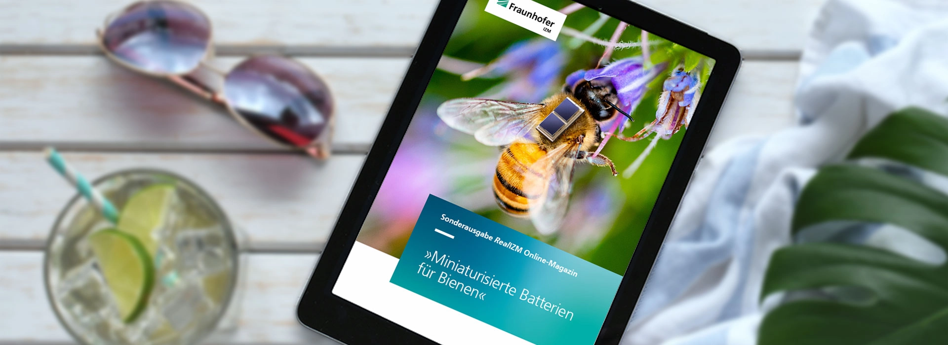 Tablet mit dem Titelbild des RealIZM Online-Magazins auf einem Steck mit Sonnenbrille, Cocktail und Pflanze | © Fraunhofer IZM | Volker Mai | MargJohnsonVA – stock.adobe