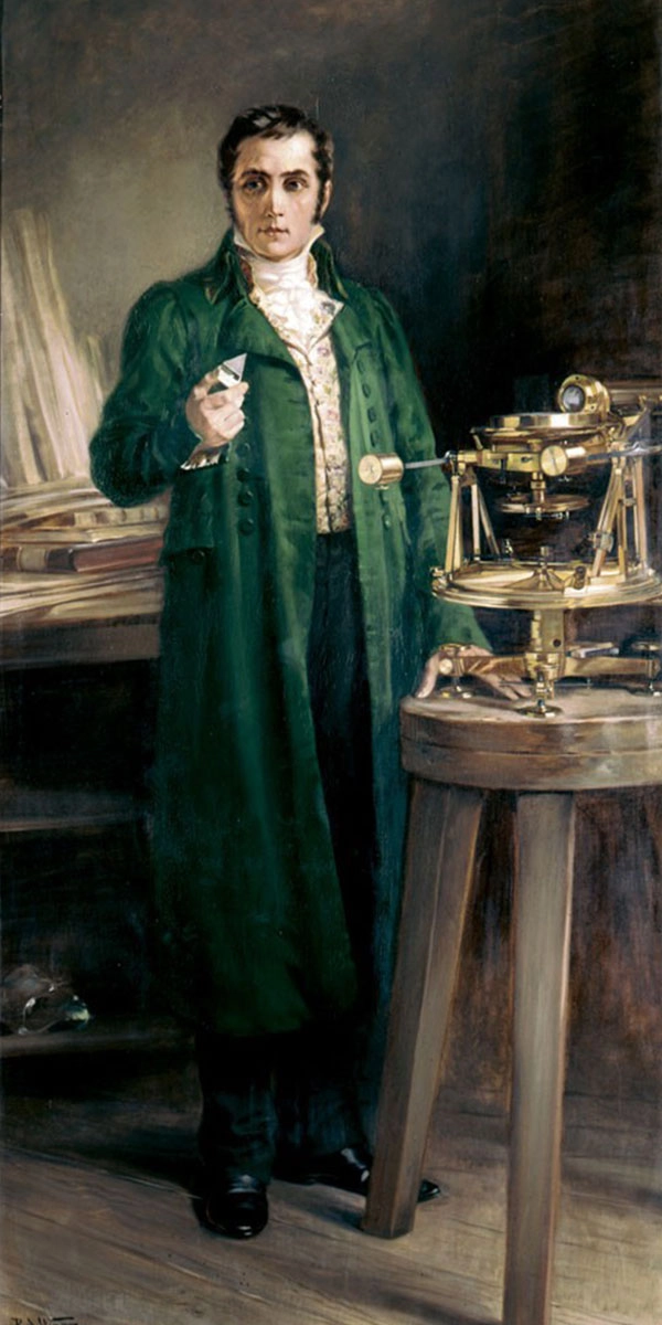 Portrait of Joseph von Fraunhofer wearing a green coat, standing beside a historic spectrometer on a wooden table. He holds an optical component in his hand and looks directly at the viewer.