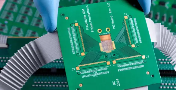 A gloved hand holds a green printed circuit board (PCB) above other electronic circuit boards with connectors and ribbon cables, set against a dramatically cloudy background.